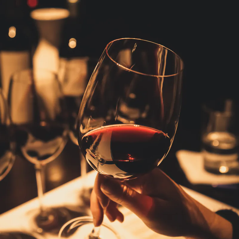 A hand raising a glass of red wine across a candlelit table.